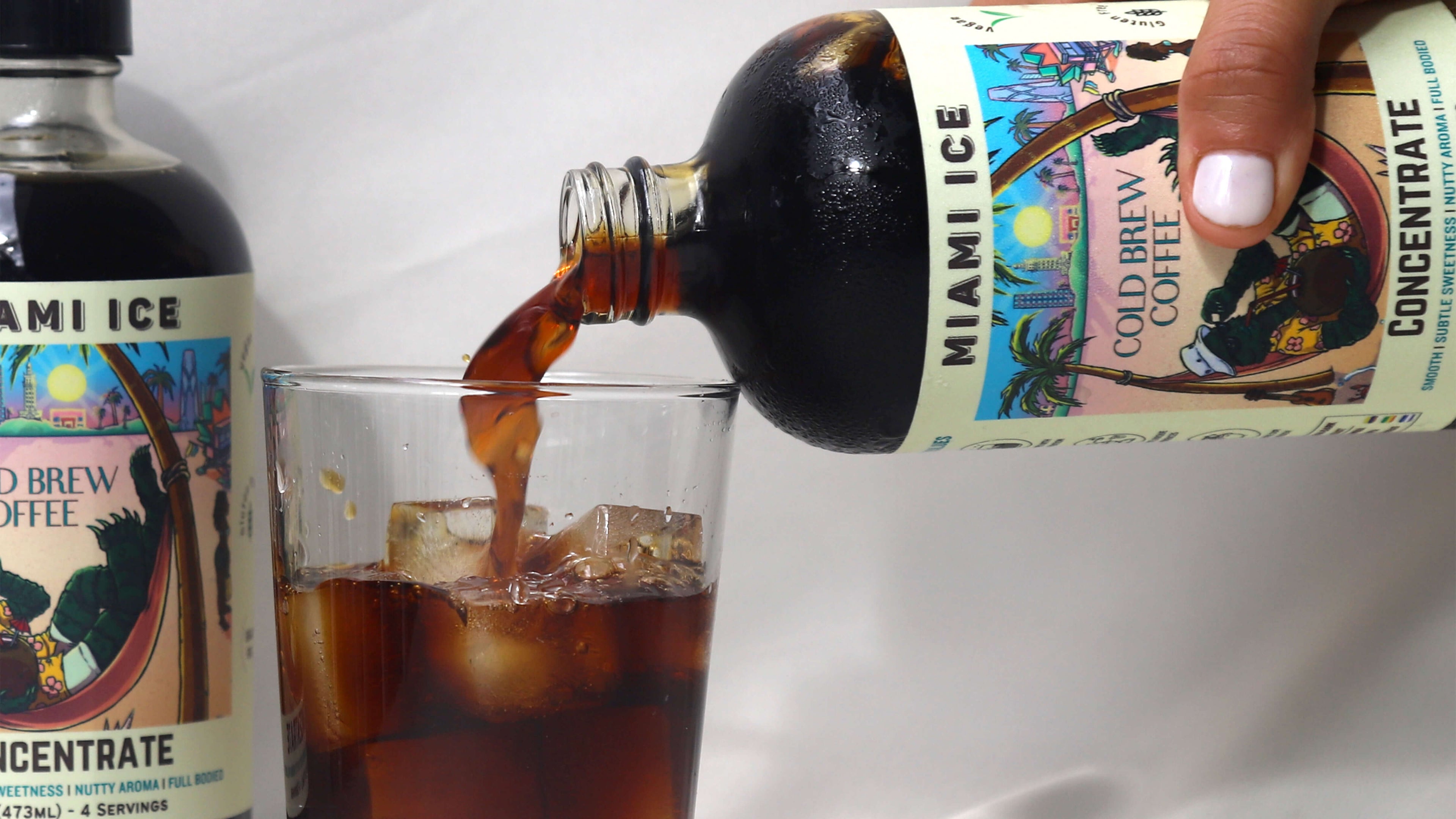 Bottle of cold brew concentrate being pouted into a clear glass cup of ice.